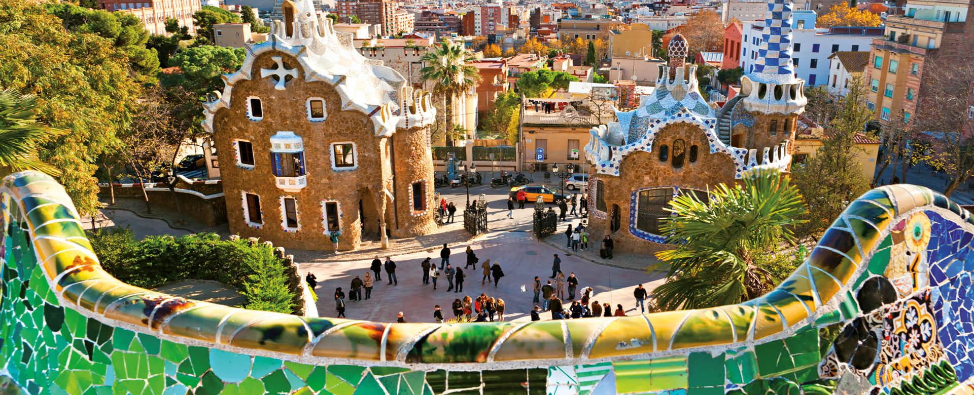 Park Güell mit Gaudí-Architektur und Blick über Barcelona Park Güell in Barcelona mit farbenfroher Mosaikbank im Vordergrund, den markanten Gebäuden von Antoni Gaudí und Blick über die Stadt bis zum Meer
