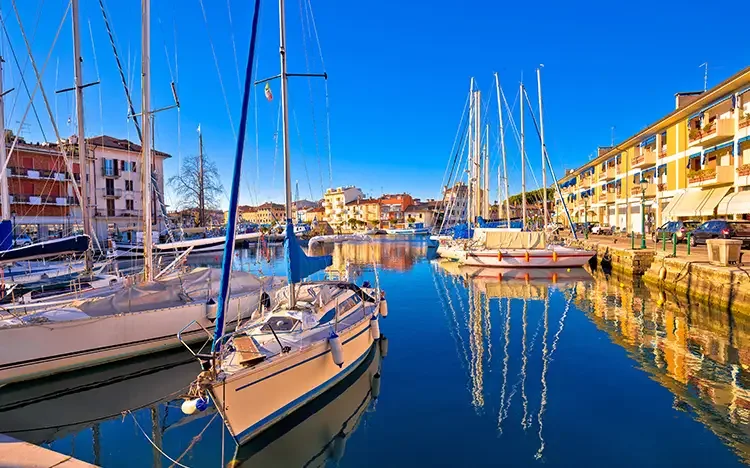 Segelboote im Hafen von Grado mit ruhigem Wasser, Spiegelungen und mediterranen Häusern im Herbstlicht