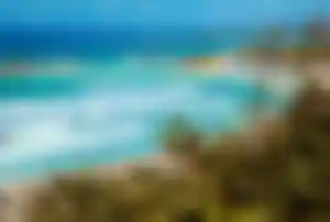 Traumstrand auf Zypern mit türkisblauem Wasser, Palmen, Sonnenschirmen und Blick auf Hotelanlagen am Meer