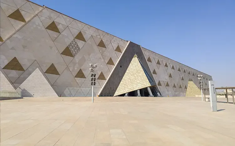 Moderne Museumsarchitektur des Grand Egyptian Museum mit geometrischer Fassade und weitem Vorplatz unter blauem Himmel.