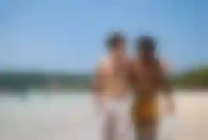 Zwei Personen spazieren gemeinsam an einem Sandstrand entlang der Küste von Mykonos