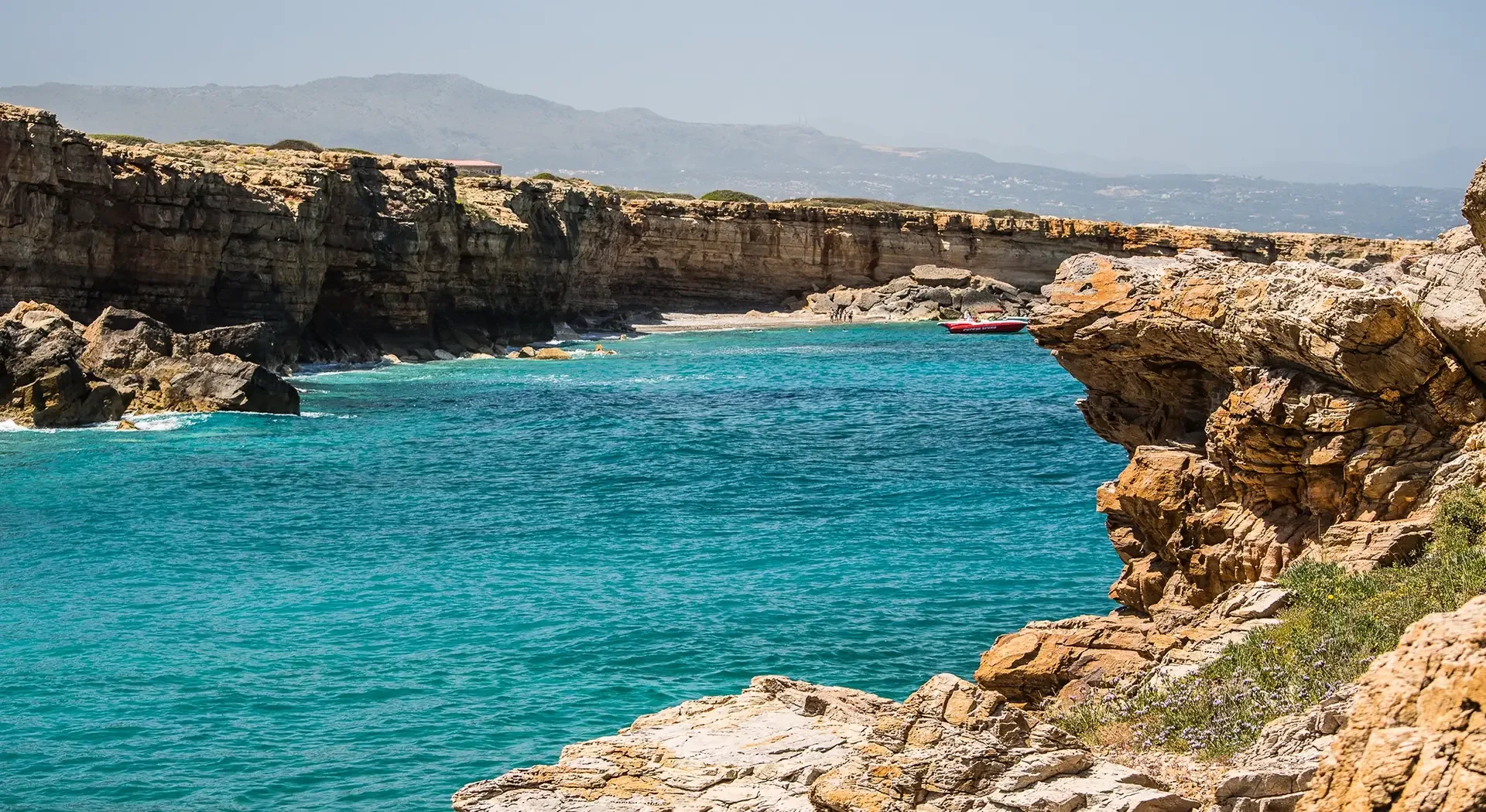 Felsige Meeresbucht mit türkisblauem Wasser, steilen Klippen und kleinem Boot vor der Küste Kretas
