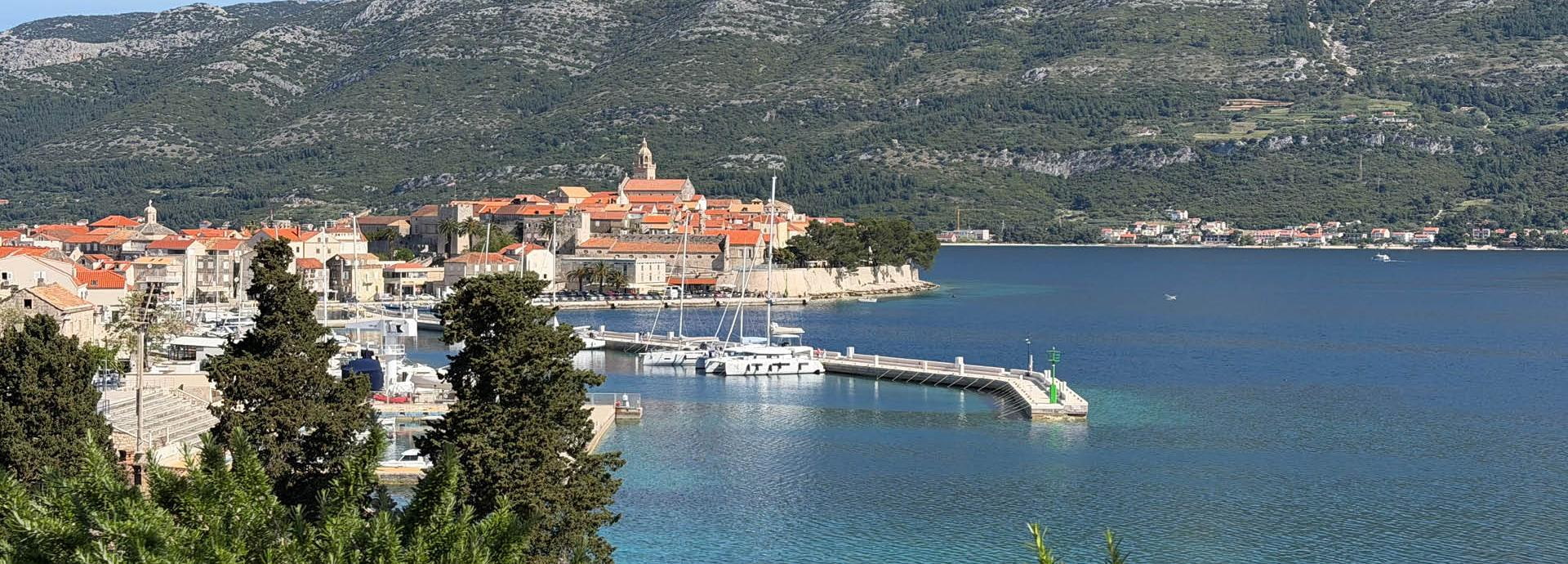 Panoramablick auf die Altstadt von Korčula mit Hafen, türkisblauem Meer und Bergen im Hintergrund in Kroatien
