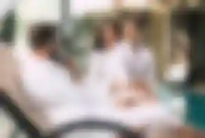 Drei Personen in weißen Bademänteln sitzen gemeinsam in einer Wellnessanlage am Pool auf einer Liege und unterhalten sich.