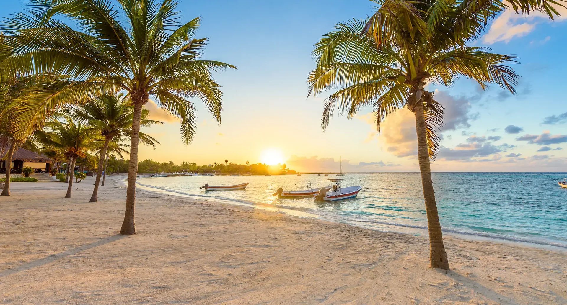 Tropischer Sandstrand in Mexiko mit Palmen, Booten und türkisblauem Meer bei Sonnenuntergang