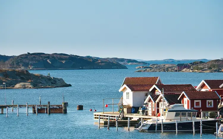 Rote Holzhäuser am Wasser mit Booten und felsiger Küstenlandschaft in der Schärenregion bei Göteborg.