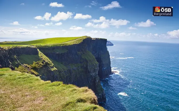 Eindrucksvolle Cliffs of Moher an der irischen Atlantikküste mit grünen Wiesen und blauem Meer.