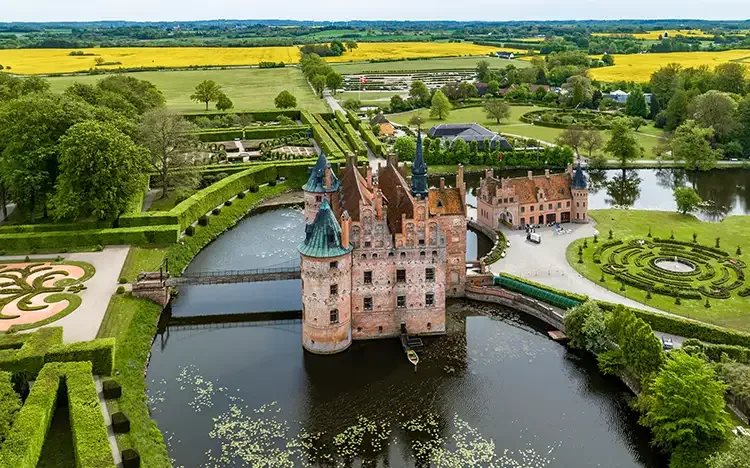 Luftaufnahme von Schloss Egeskov mit Wassergraben, Gartenanlagen und umliegender Landschaft.