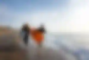  Zwei Surfer mit Boards laufen am Strand entlang