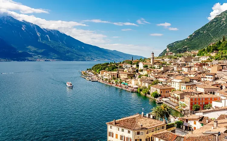 Limone sul Garda am Gardasee mit bunten Häusern, Seeufer und umliegenden Bergen unter blauem Himmel