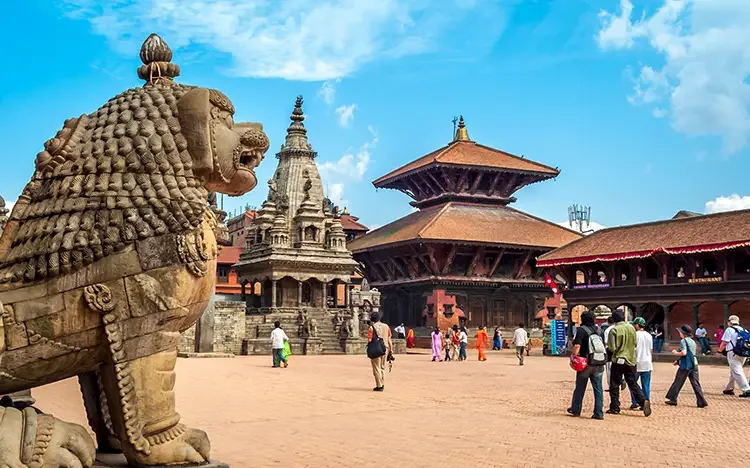 Historischer Platz in Bhaktapur mit steinernem Löwen und traditionellen Tempeln unter blauem Himmel.