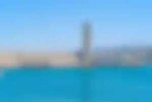 Historischer Leuchtturm auf einer steinernen Hafenmole mit kleinen Booten und türkisblauem Meer vor der Küste von Rethymno