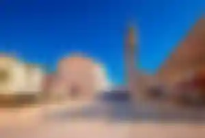 Offener Platz in Umag mit historischer Kirche, Glockenturm, Cafés und mediterranen Gebäuden unter klarem Himmel, typisch für die Küstenregion in Istrien.