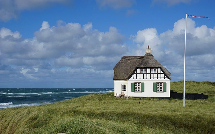 Reetgedecktes Haus in den Dünen mit Blick auf die Nordsee und dänischer Flagge.