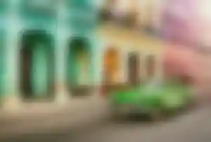 Grüner Oldtimer fährt durch eine Straße mit bunten Kolonialgebäuden und verzierten Balkonen in Havanna