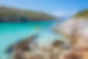 Türkisfarbene Bucht in Griechenland mit klarem Wasser, Felsenküste und einem Kajak auf dem Meer.