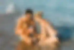 Zwei Erwachsene und ein Kind sitzen im flachen Wasser am Strand und spielen in den sanften Wellen