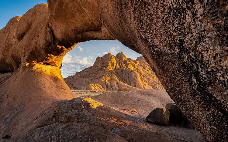 Felsformation Spitzkoppe in Namibia, durch einen natürlichen Steinbogen fotografiert bei Sonnenuntergang.