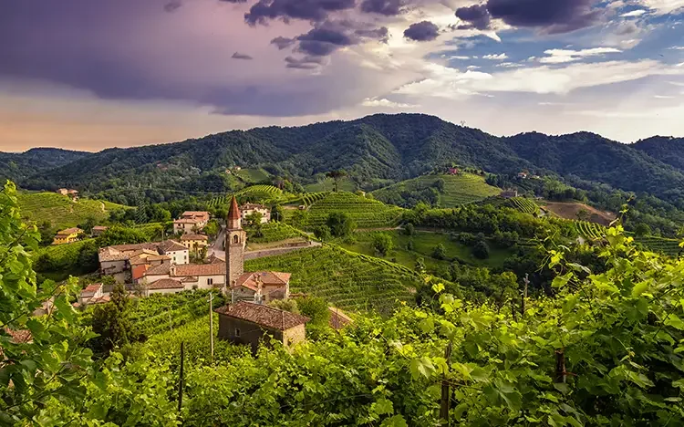 Idyllische Landschaft der Prosecco‑Straße mit sanften Hügeln, Weinbergen und Dorfkirche.