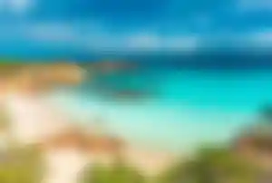 Weiße Sandbucht auf Sardinien mit kristallklarem türkisfarbenem Wasser, Felsen und mediterraner Küstenlandschaft.
