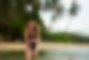 Frau steht mit schwarzem Badeanzug und einer roten Blume im offenen Haar im Meer vor einem Strand in Bali