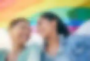 Zwei Personen stehen unter einer Regenbogenflagge und blicken sich gemeinsam an