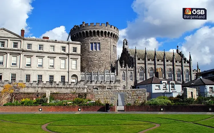 Dublin Castle mit mittelalterlichem Turm und Garten unter blauem Himmel.