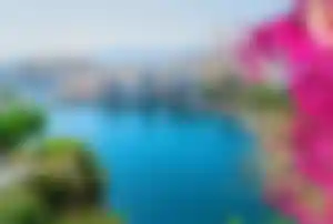 Blick auf den Hafen von Agios Nikolaos auf Kreta mit türkisblauem Wasser, Booten und blühenden Bougainvillea im Vordergrund