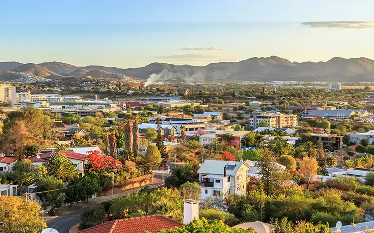 Stadtansicht von Windhoek mit Wohnhäusern, grünen Bäumen und Bergen im Hintergrund.