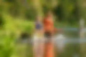 Mutter und Tochter sitzen auf einem Steg, lachen und spritzt Wasser in einer sonnigen Seenlandschaf