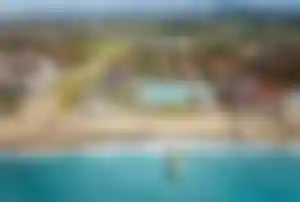 Luftaufnahme eines Strandresorts mit großem Pool, Palmen, Steg ins Meer und Hotelgebäuden vor einer bergigen Landschaft an der türkischen Küste.