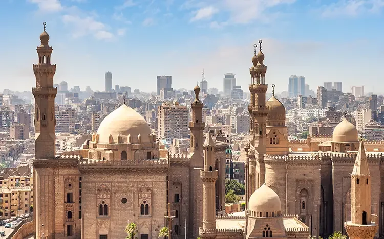 Historische Moscheen mit Kuppeln und Minaretten im Stadtzentrum von Kairo, im Hintergrund moderne Hochhäuser und dichte Bebauung.