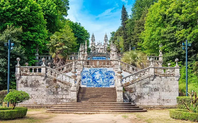 Prunkvolle barocke Treppenanlage mit blau-weißen Azulejo-Fliesen, umgeben von üppigem Grün und Bäumen in Lamego.