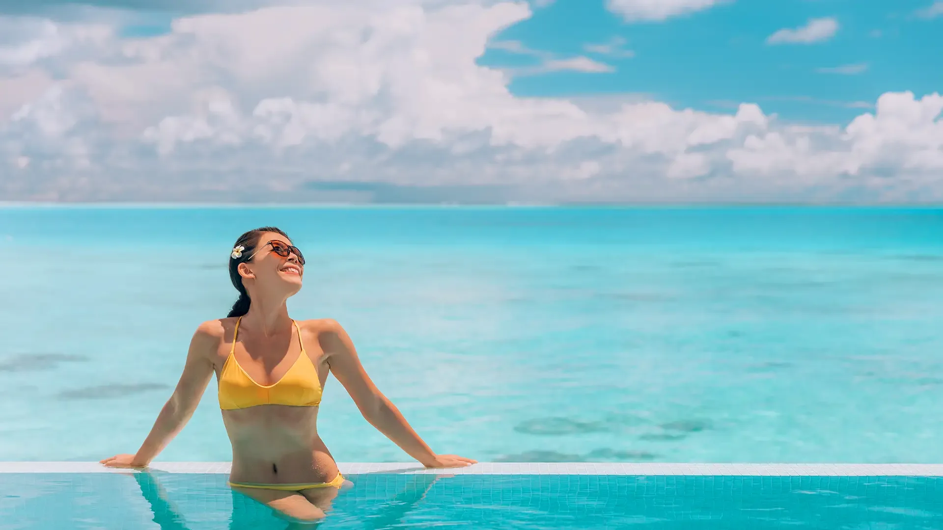 Frau in gelben Bikini genießt ihren verlängerten Sommer in einem Infinity Pool