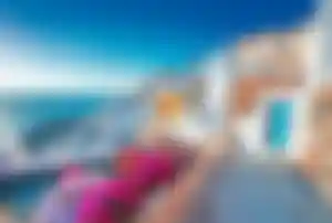 Typische weiße Häuser von Santorini mit Blick auf das Ägäische Meer und blühende Blumen entlang eines Küstenwegs.