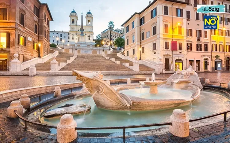 Spanische Treppe in Rom mit Brunnen im Vordergrund und Kirche Trinità dei Monti im Hintergrund bei Abendbeleuchtung.