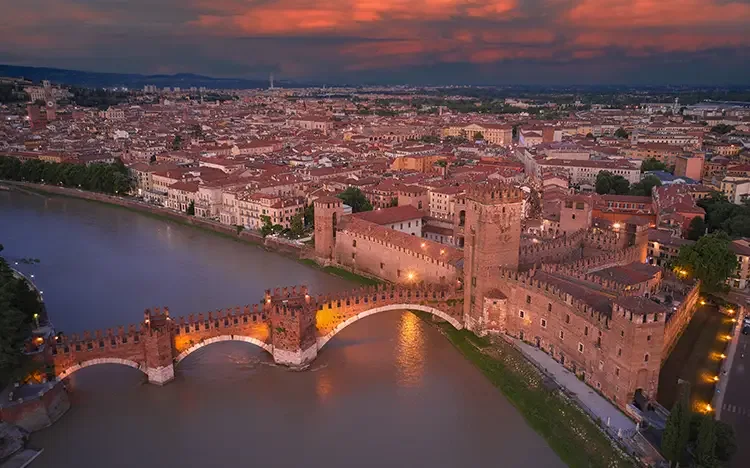 Atemberaubender Blick auf Verona mit der beleuchteten Ponte di Castelvecchio bei Sonnenuntergang.