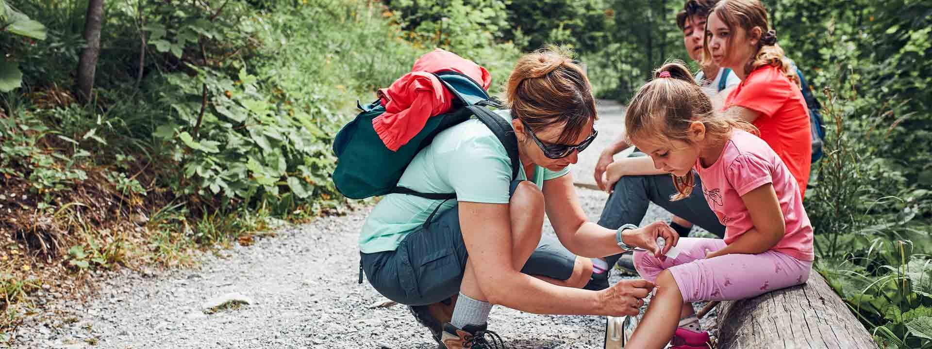 Familienurlaub Reiseapotheke Mutter, die die Wunde auf dem Knie ihrer kleinen Tochter verarztet
