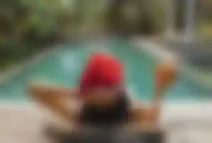 Frau mit Weihnachtsmütze entspannt auf einer Liege am Pool und hält eine Kokosnuss in der Hand – Symbolbild für Weihnachten unter Palmen und Urlaub zu Weihnachten im Warmen.