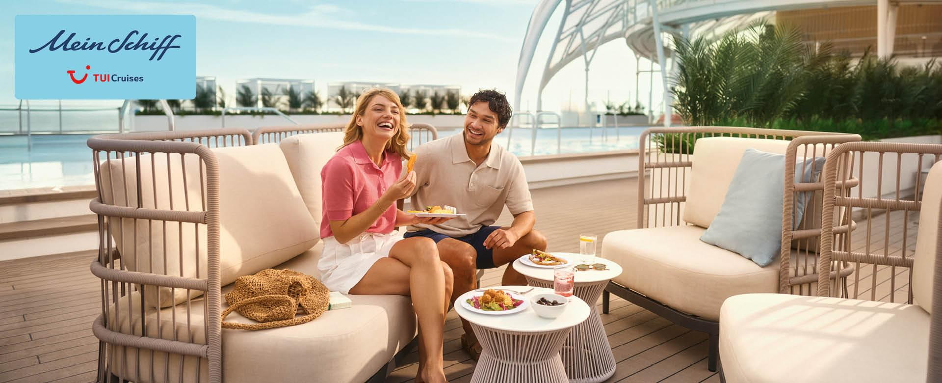 Pärchen sitz an Deck der Mein Schiff Flow und genießt Snacks an Board