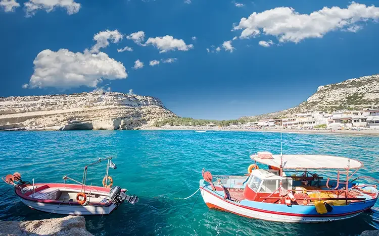 Fischerboote im türkisfarbenen Wasser vor den Felsen von Matala auf Kreta.