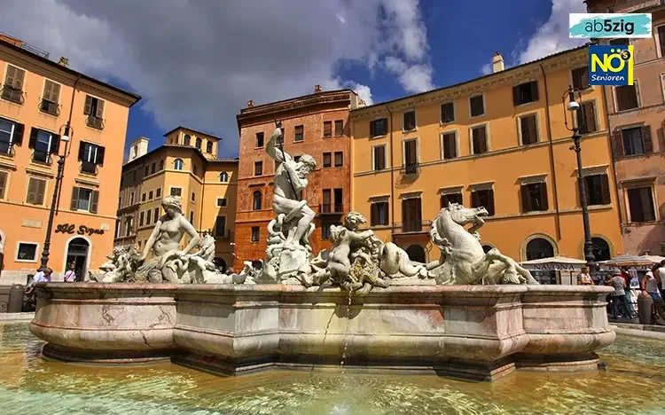Barockbrunnen auf der Piazza Navona in Rom, umgeben von historischen Gebäuden unter blauem Himmel mit Wolken.