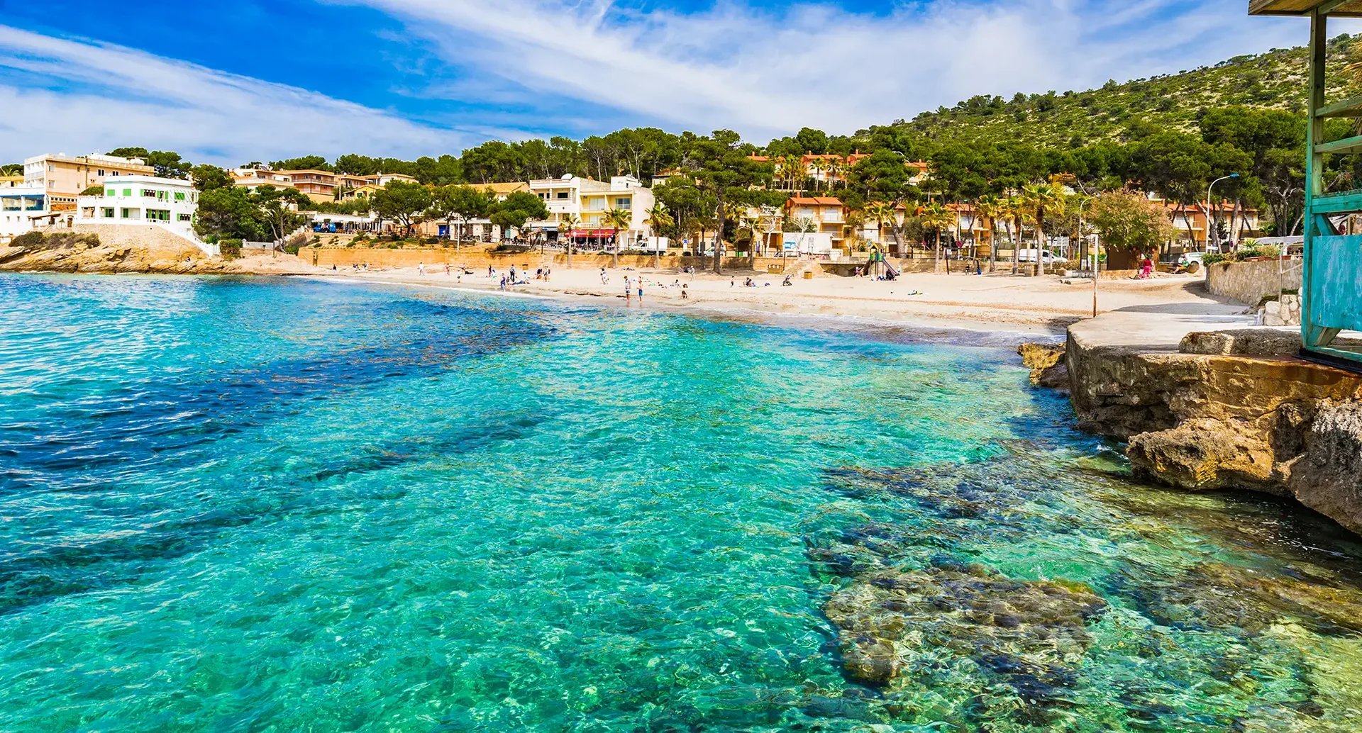 Strand von Sant Elm mit klarem Wasser, Felsen und Küstenpromenade auf Mallorca