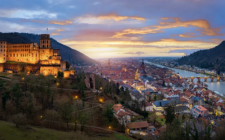 Heidelberg: abendlicher Panoramablick auf die Schlossruine und die Altstadt mit Weihnachtsmarkt auf dem Marktplatz.