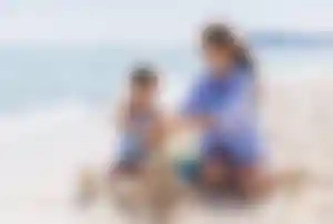 Person und Kind bauen Sandburgen an einem Sandstrand am Meer mit Eimer und Sandspielzeug