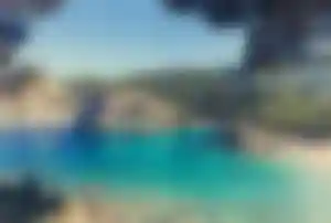 Türkisblaue Bucht auf Korfu mit felsiger Küste, klarem Wasser und grünen Hügeln im Hintergrund
