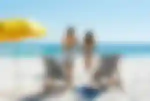 Zwei Sonnenliegen und Sonnenschirm am Strand, Blick auf das Meer als Symbol für günstige Pauschalreisen
