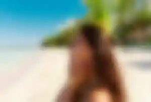 Person steht an einem weißen Sandstrand mit Palmen und Meer im Hintergrund, typisches Motiv für Low Budget Reiseziele mit Sonne und Strand