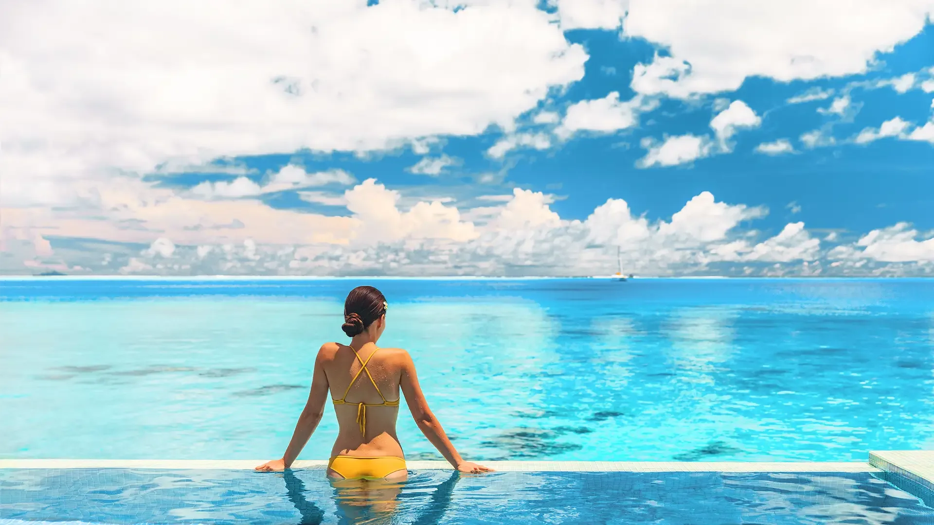 Frau in gelben Bikini genießt den Ausblick aufs Meer während sie im Infinity Pool steht