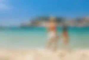 Frau und ihre kleine Tochter im Badeanzug stehen zusammen am Strand und beobachten die Bucht von Soller auf Mallorca.